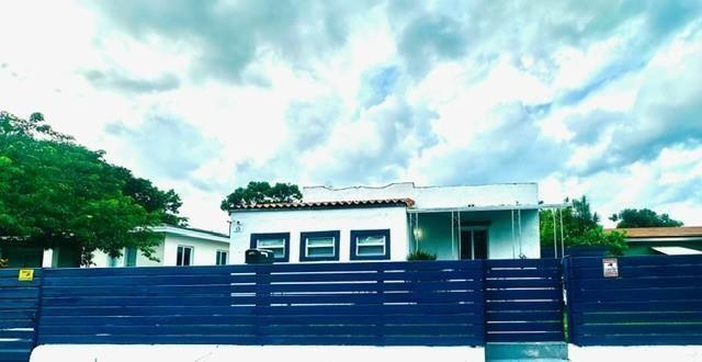 A white single-story house with a blue horizontal slat fence in the foreground — 55 NW 47th Street, Miami FL 33127, MIAMI, FL