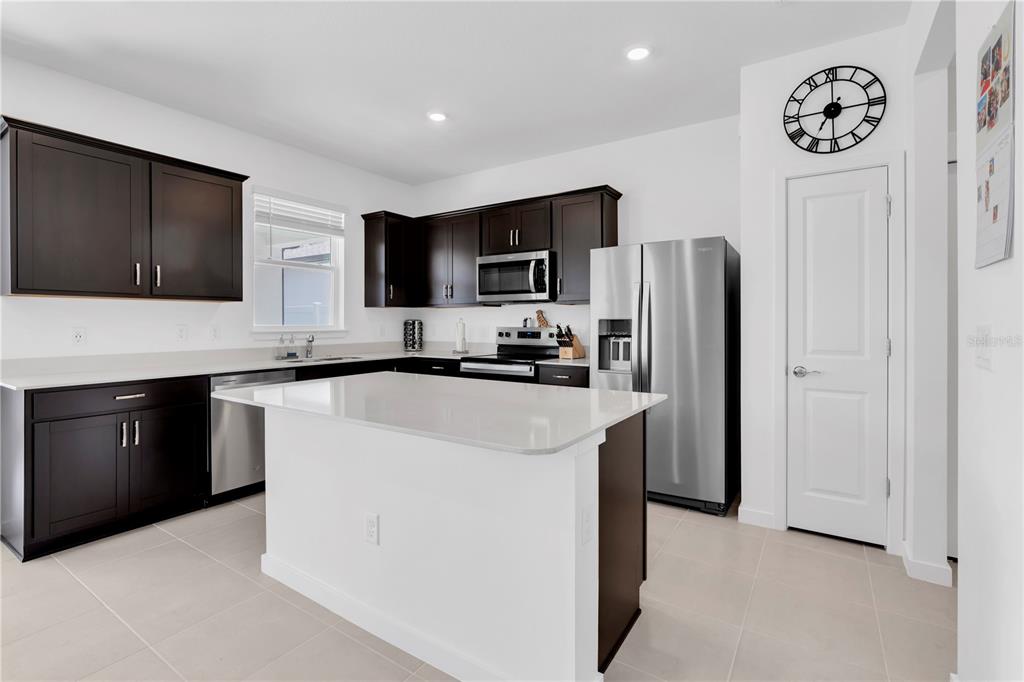 A kitchen features dark wood cabinets, white countertops, a central island, and stainless steel appliances — 4199 BIG SKY DRIVE, SPRING HILL, FL