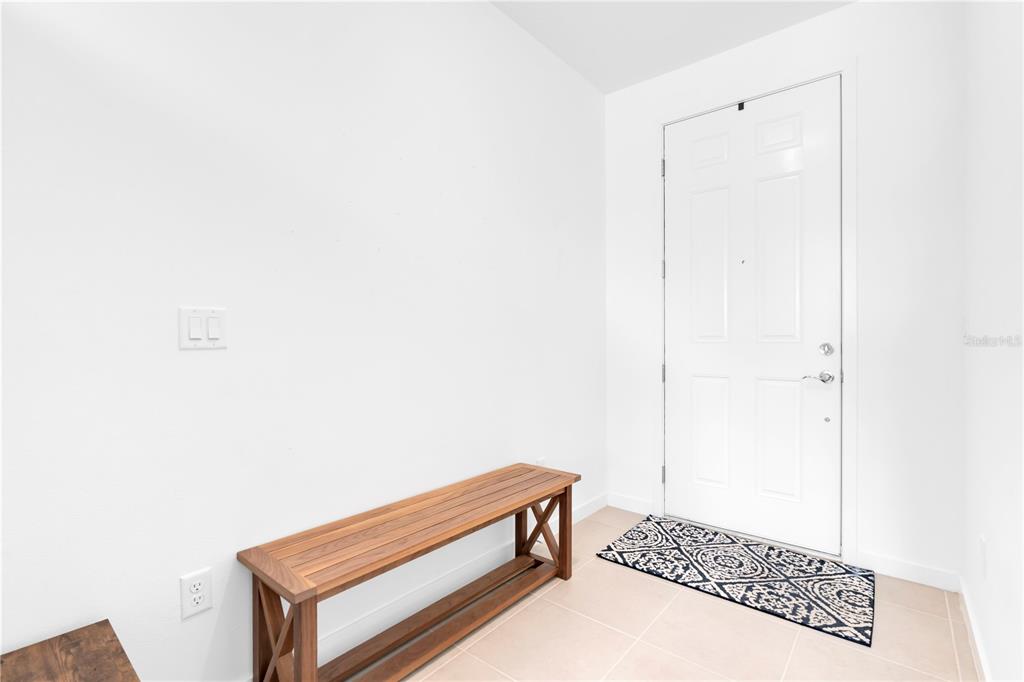 An entryway features a wooden bench, a patterned rug, and a white door on tile flooring — 4199 BIG SKY DRIVE, SPRING HILL, FL