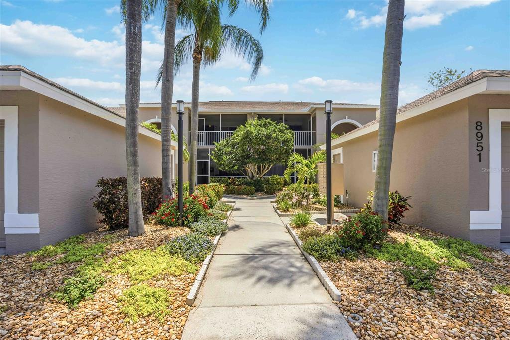 A concrete walkway leads to the entrance of a two-story residential building with palm trees — 8951 VERANDA WAY UNIT 623, SARASOTA, FL