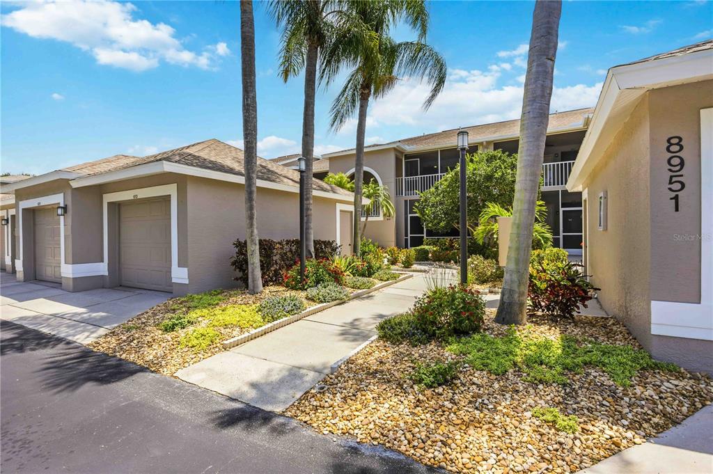 A tan multi-unit building exterior with a walkway, palm trees, and a garage — 8951 VERANDA WAY UNIT 623, SARASOTA, FL