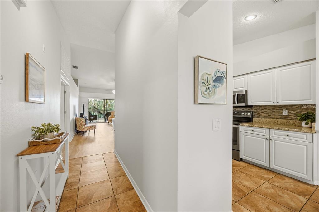 A tiled hallway leads to a living area with a balcony view and an adjacent kitchen — 8951 VERANDA WAY UNIT 623, SARASOTA, FL