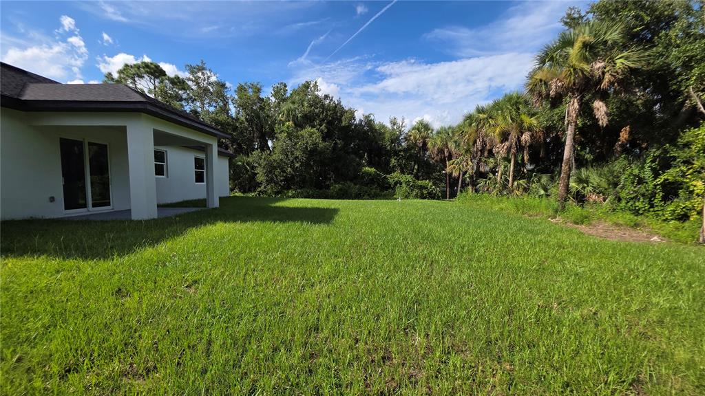 A view of a grassy backyard with a covered patio and surrounding palm trees — 286 KRIEGER STREET, PORT CHARLOTTE, FL