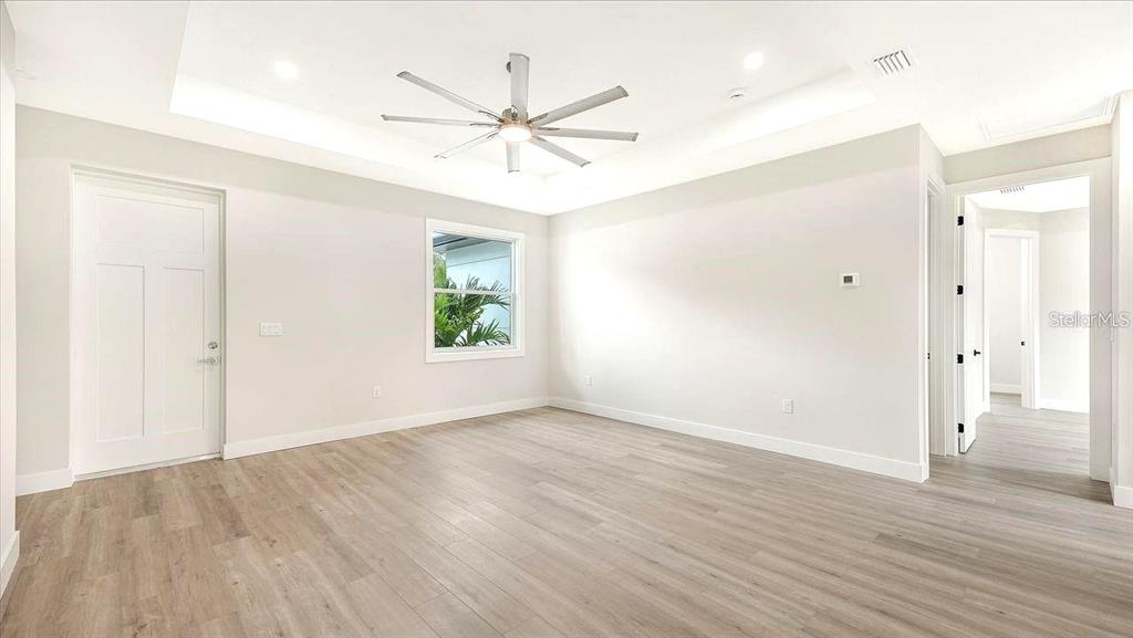 An empty bedroom features light wood-look flooring, a tray ceiling with a fan, and white walls — 286 KRIEGER STREET, PORT CHARLOTTE, FL