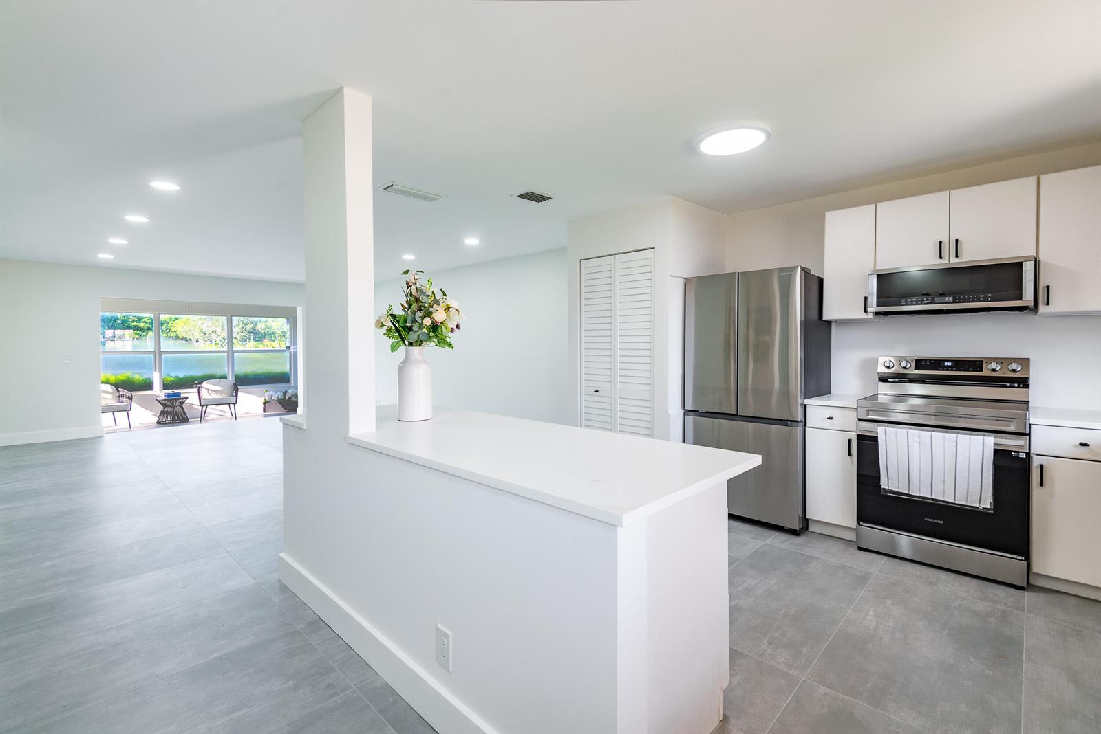A modern kitchen with white cabinets, stainless steel appliances, and a breakfast bar overlooks a patio — 604 Laconia Circle, Lake Worth FL 33467, LAKE WORTH, FL