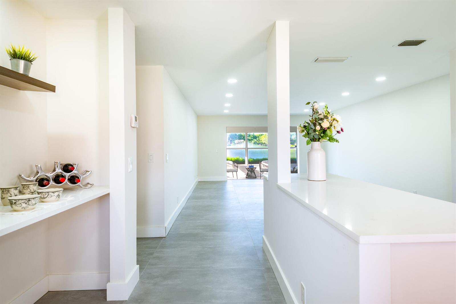 A bright hallway with gray tile flooring leads toward a windowed view of a patio — 604 Laconia Circle, Lake Worth FL 33467, LAKE WORTH, FL