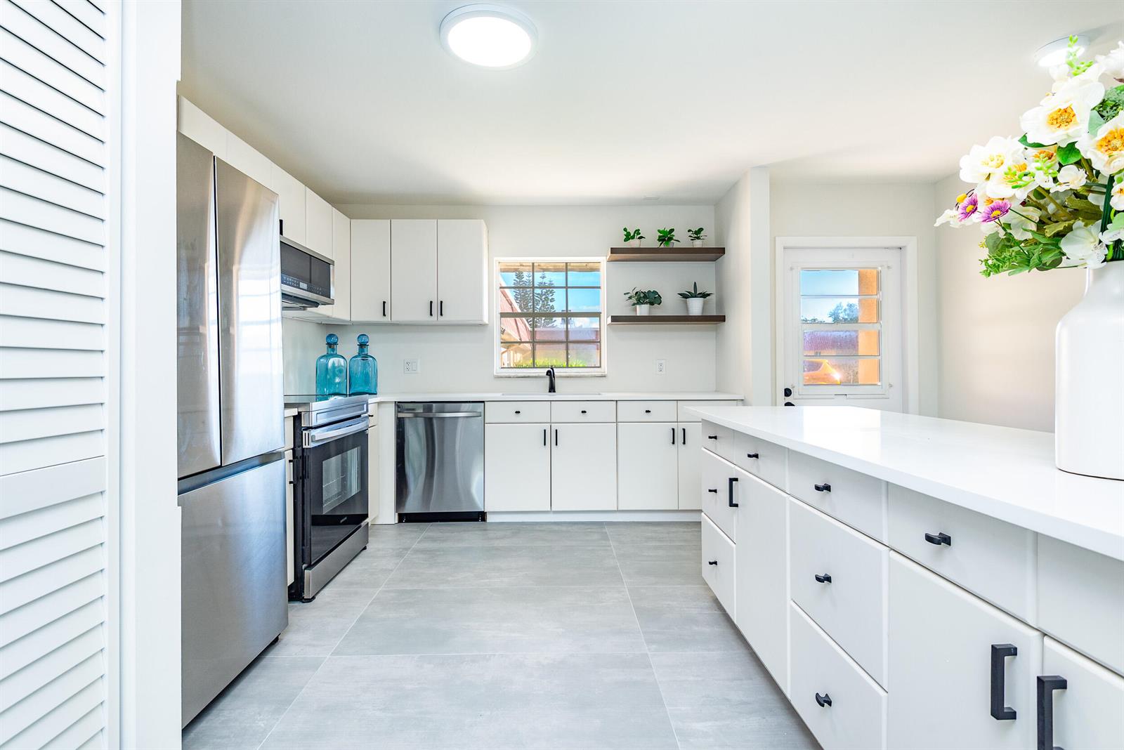 A modern kitchen features white cabinets, stainless steel appliances, gray tile floors, and open shelving — 604 Laconia Circle, Lake Worth FL 33467, LAKE WORTH, FL