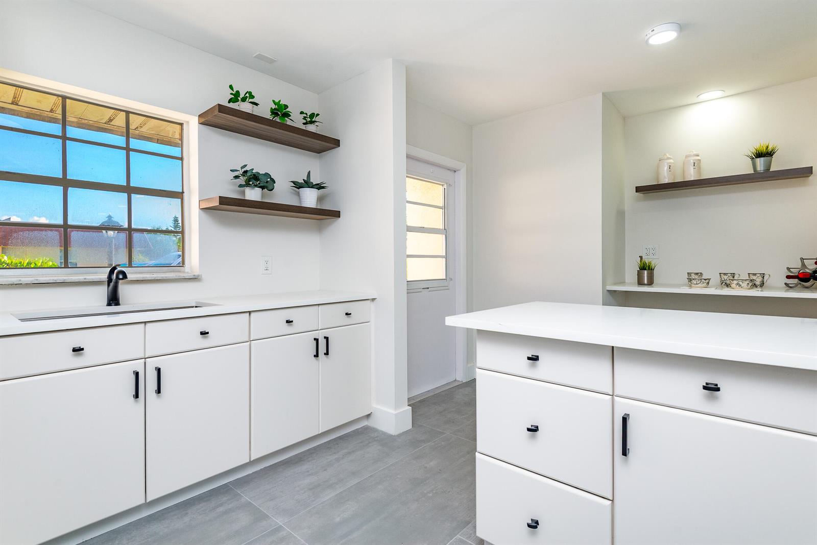 A kitchen features white cabinets, a central island, floating shelves, and a window above the sink — 604 Laconia Circle, Lake Worth FL 33467, LAKE WORTH, FL