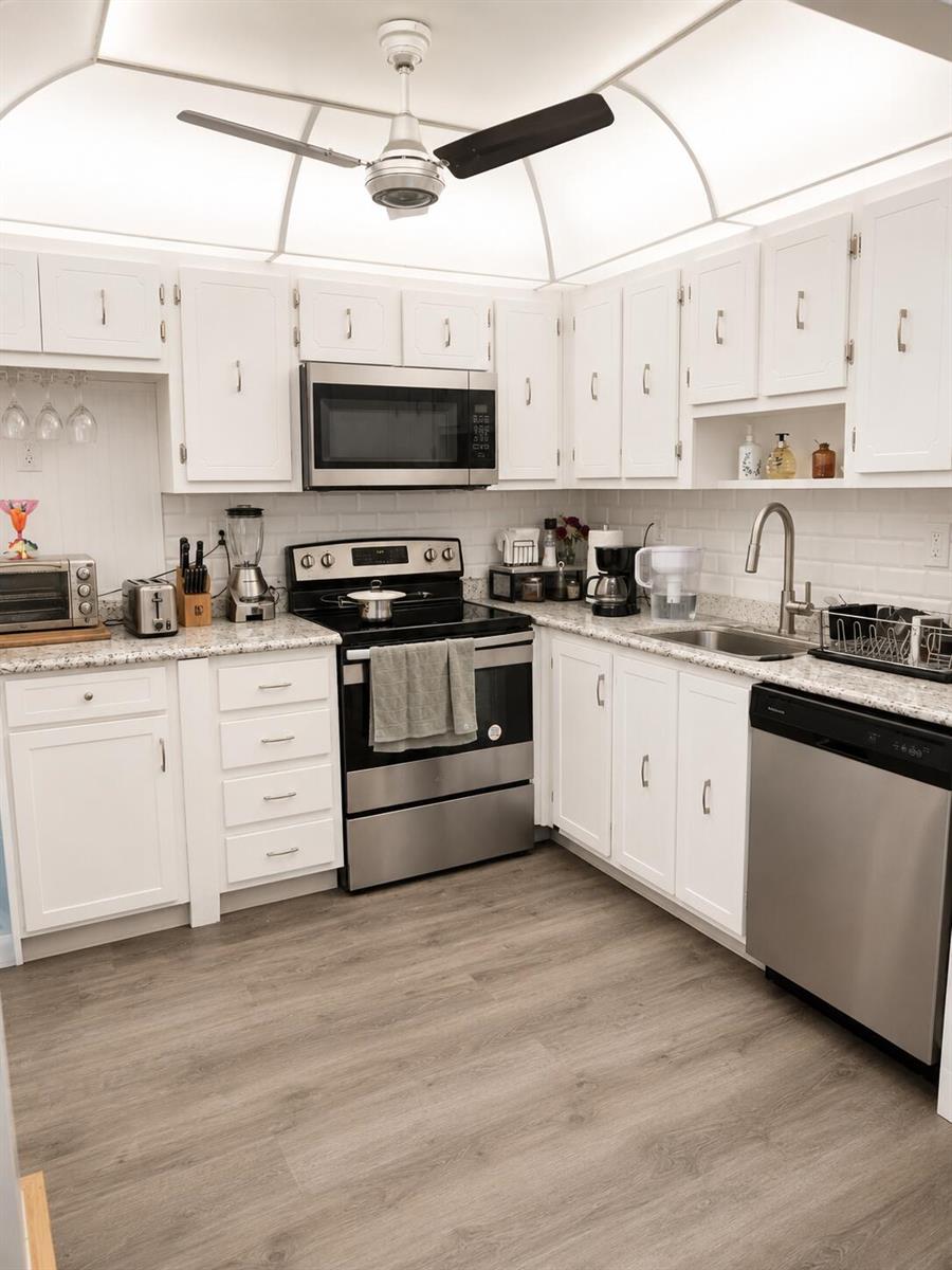 A kitchen with white cabinets, stainless steel appliances, granite countertops, and wood-look flooring — 415 Normandy Lane # I, Delray Beach FL 33484, DELRAY BEACH, FL