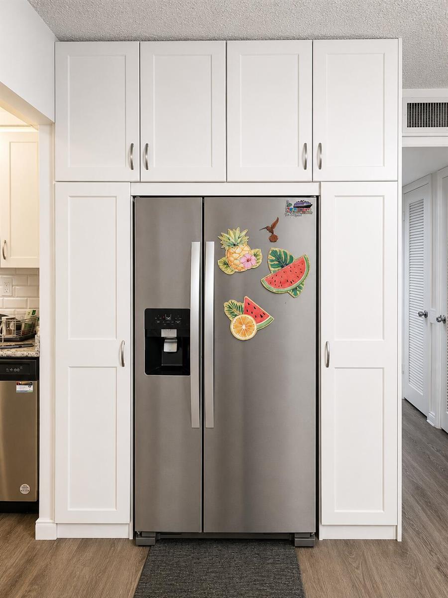 A stainless steel refrigerator is framed by white cabinetry in a kitchen with wood flooring — 415 Normandy Lane # I, Delray Beach FL 33484, DELRAY BEACH, FL