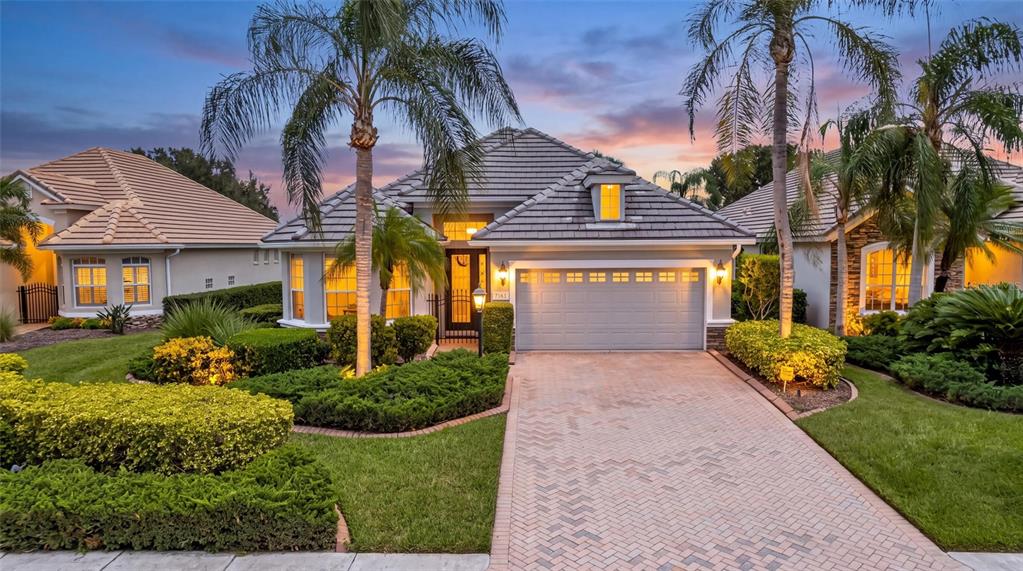 A single-story house with a tiled roof, a paved driveway, and palm trees at dusk — 7163 SANDHILLS PLACE, LAKEWOOD RANCH, FL
