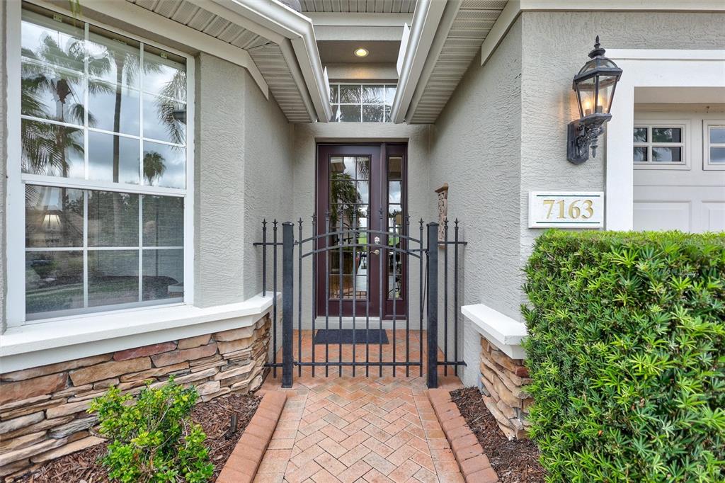 A brick walkway leads to a front door enclosed by a black metal gate — 7163 SANDHILLS PLACE, LAKEWOOD RANCH, FL
