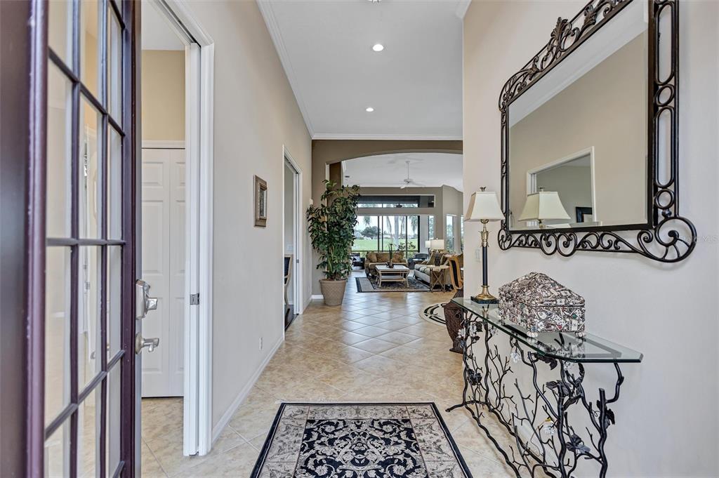 A foyer with tile flooring leads into a living room with a view of the outdoors — 7163 SANDHILLS PLACE, LAKEWOOD RANCH, FL