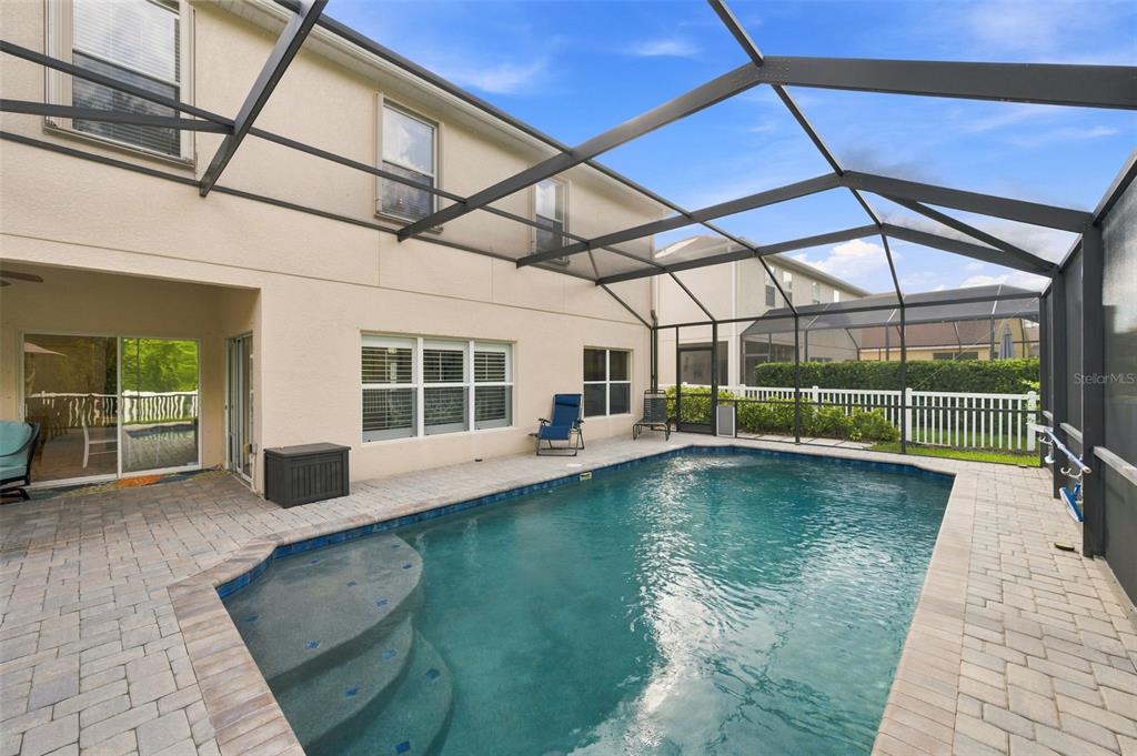 A swimming pool with a screened-in enclosure sits on a paved patio behind a house — 11507 BELLE HAVEN DRIVE, NEW PORT RICHEY, FL