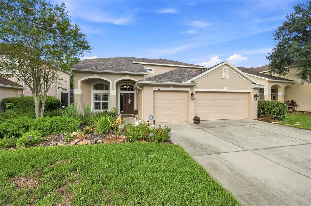 A single-story suburban house with a tan stucco exterior, a three-car garage, and landscaping — 11507 BELLE HAVEN DRIVE, NEW PORT RICHEY, FL
