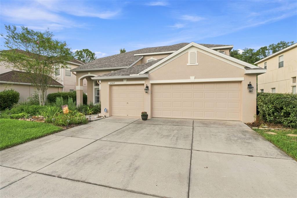A tan, single-story suburban house features a three-car garage and a concrete driveway — 11507 BELLE HAVEN DRIVE, NEW PORT RICHEY, FL