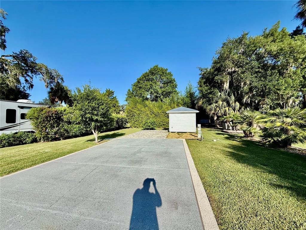 A paved driveway leads to a small storage shed in a grassy, tree-lined outdoor space — 3054 NE 101ST TERRACE UNIT 127, SILVER SPRINGS, FL