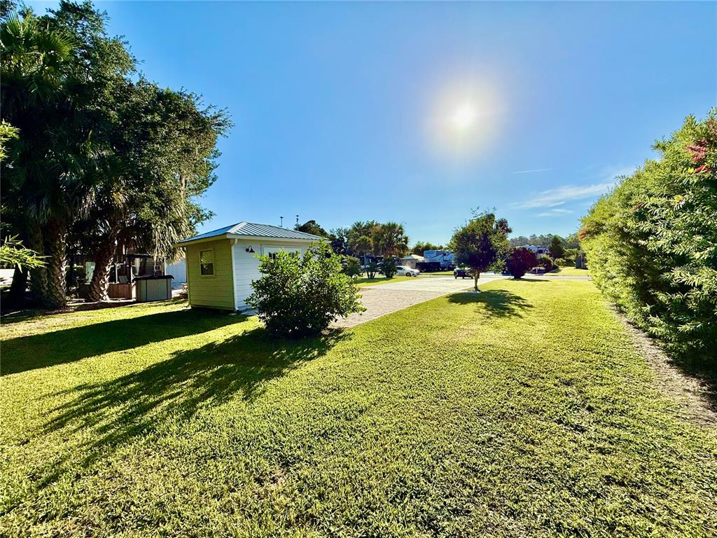 A small shed sits on a grassy lawn next to a paved driveway and trees — 3054 NE 101ST TERRACE UNIT 127, SILVER SPRINGS, FL