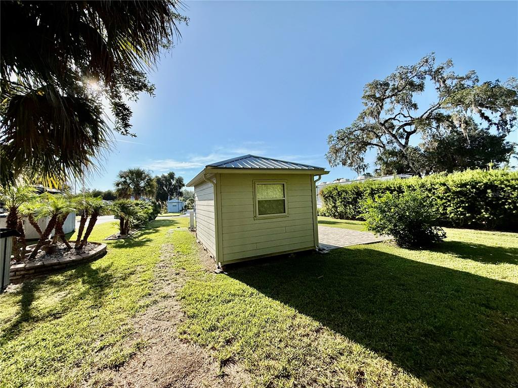 A small, light-colored shed with a metal roof sits on a grassy lawn — 3054 NE 101ST TERRACE UNIT 127, SILVER SPRINGS, FL