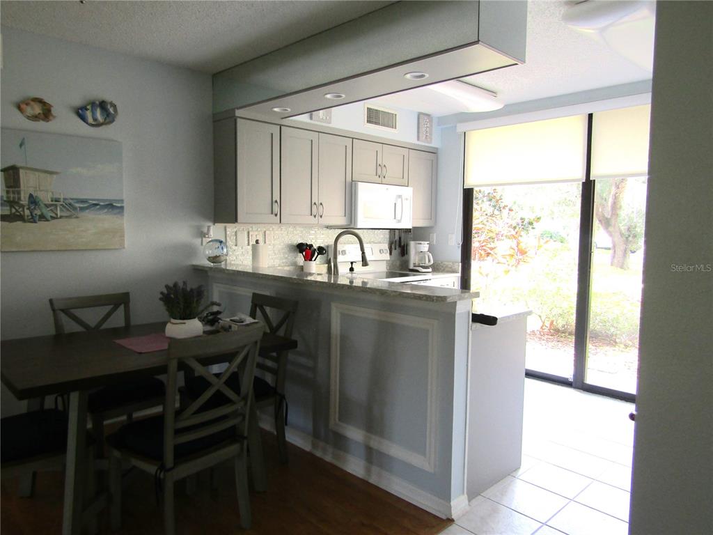 A kitchen with grey cabinets and a breakfast bar overlooks a dining area and patio — 5136 HARPERS CROFT UNIT 11, SARASOTA, FL