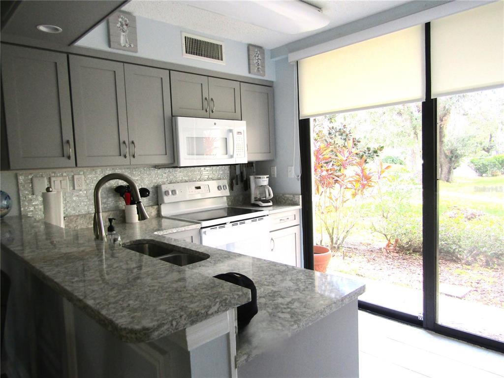 A kitchen features gray cabinets, granite countertops, white appliances, and a sliding glass door — 5136 HARPERS CROFT UNIT 11, SARASOTA, FL