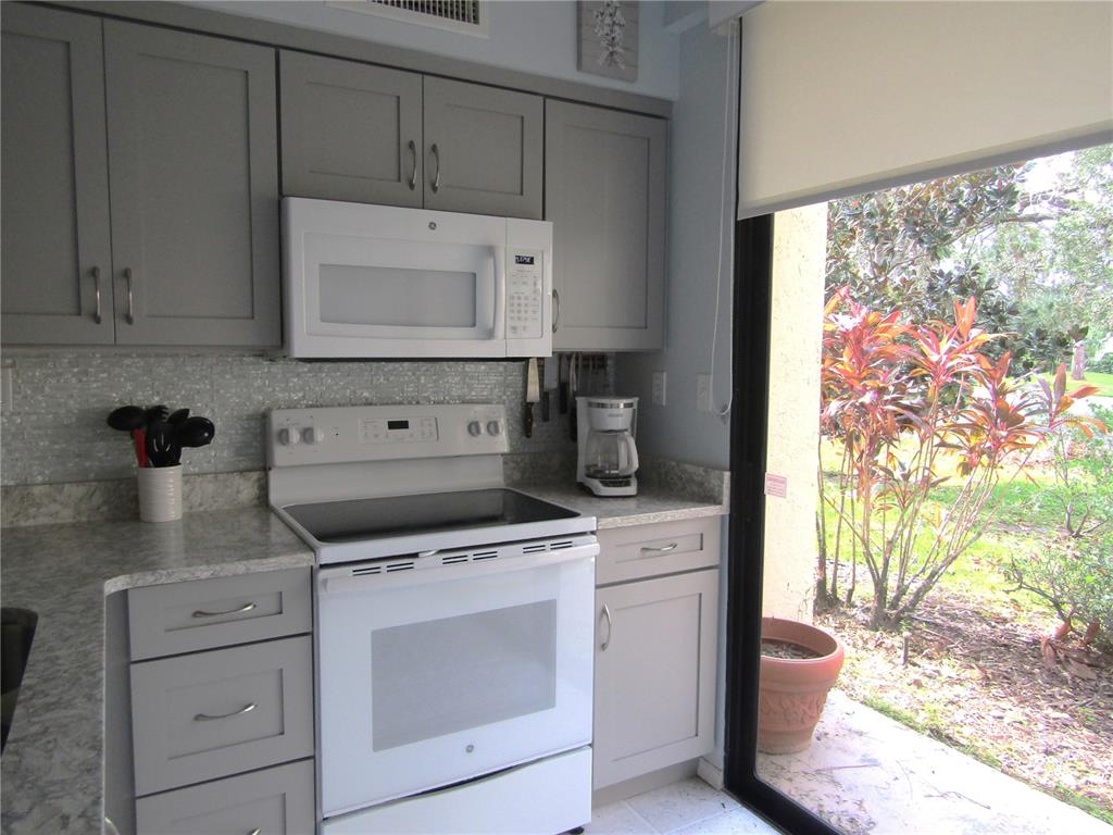 A kitchen features gray cabinets, white appliances, a tiled backsplash, and a sliding glass door — 5136 HARPERS CROFT UNIT 11, SARASOTA, FL