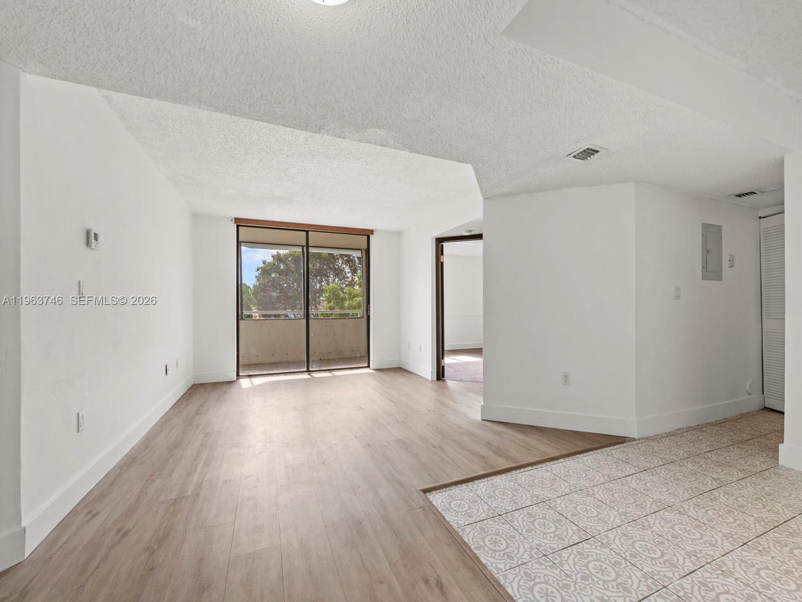 An empty living area features light wood-look flooring, white walls, and a sliding glass door — 8365 SW 152nd Ave # 310, Miami FL 33193, MIAMI, FL