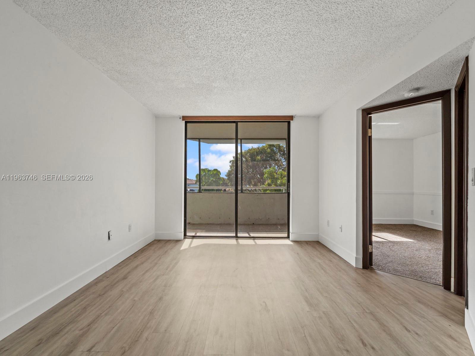 This room features light wood-look flooring, white walls, a popcorn ceiling, and a sliding glass door — 8365 SW 152nd Ave # 310, Miami FL 33193, MIAMI, FL