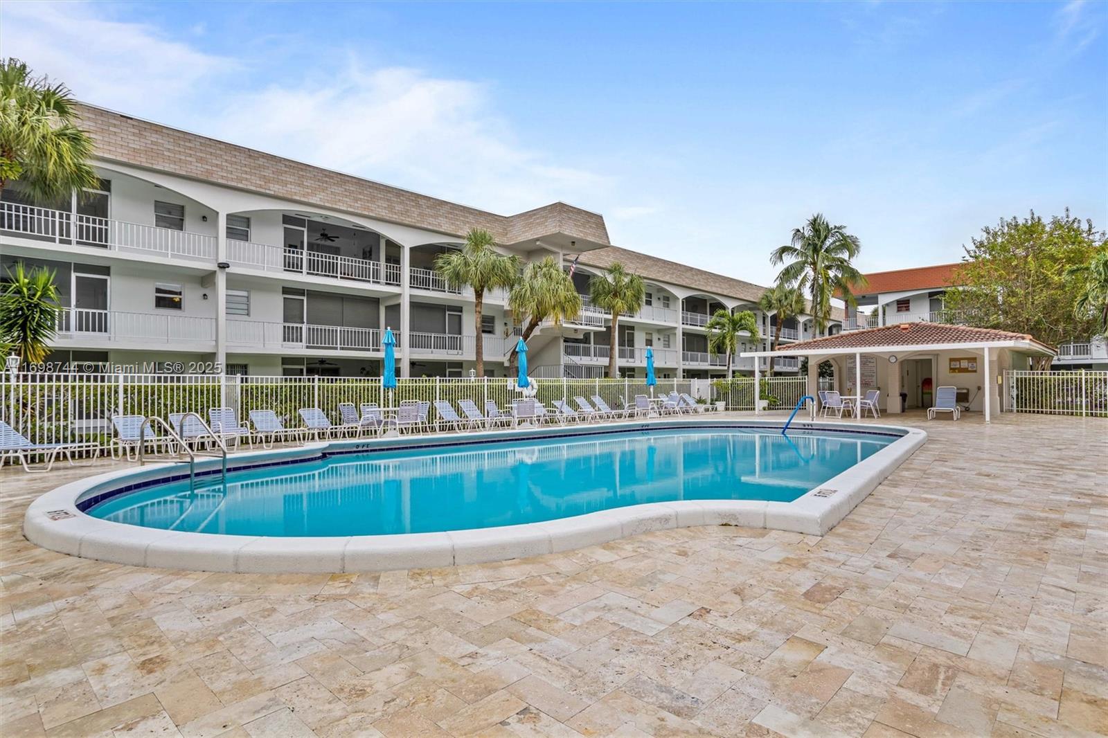 A swimming pool with lounge chairs sits in front of a multi-story apartment building — 501 Blue Heron Dr # A, Hallandale Beach FL 33009, HALLANDALE BEACH, FL