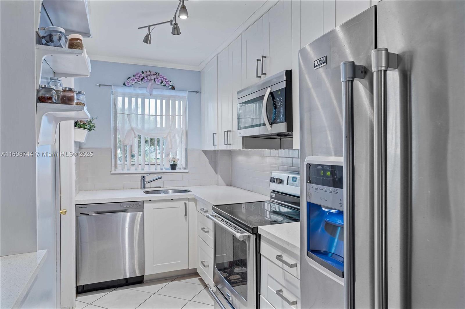 A kitchen features white cabinets, stainless steel appliances, a tiled backsplash, and a window — 501 Blue Heron Dr # A, Hallandale Beach FL 33009, HALLANDALE BEACH, FL
