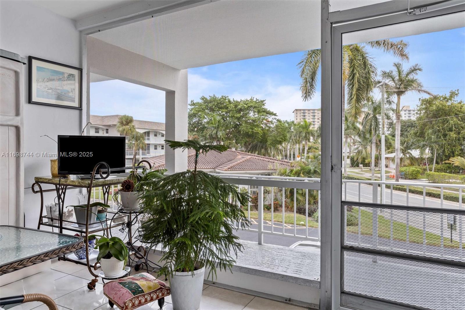 A covered balcony features a metal cart, potted plants, and a view of palm trees — 501 Blue Heron Dr # A, Hallandale Beach FL 33009, HALLANDALE BEACH, FL