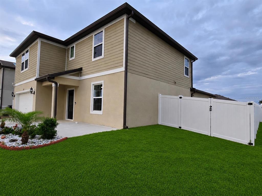 A two-story house with tan siding and stucco exterior features a white vinyl privacy fence — 1213 MICHELANGELO LANE, WINTER HAVEN, FL
