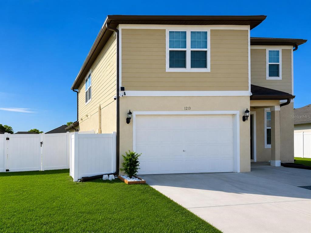 A two-story house with tan siding, a white garage door, and a white vinyl fence — 1213 MICHELANGELO LANE, WINTER HAVEN, FL