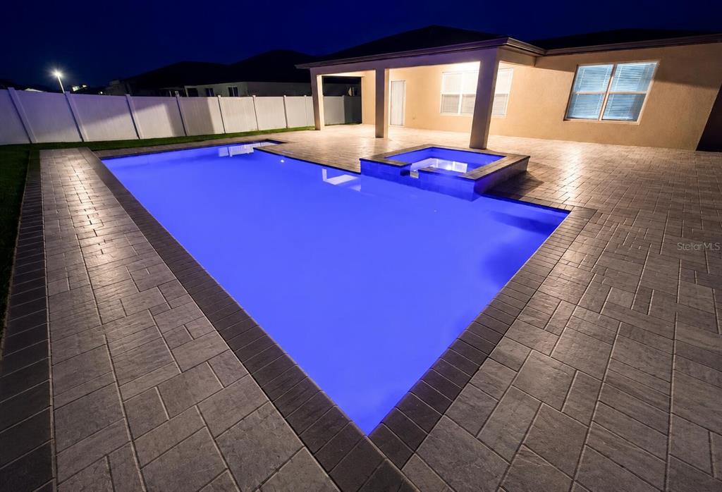 A rectangular swimming pool with an attached spa sits on a paved patio at night — 1213 MICHELANGELO LANE, WINTER HAVEN, FL