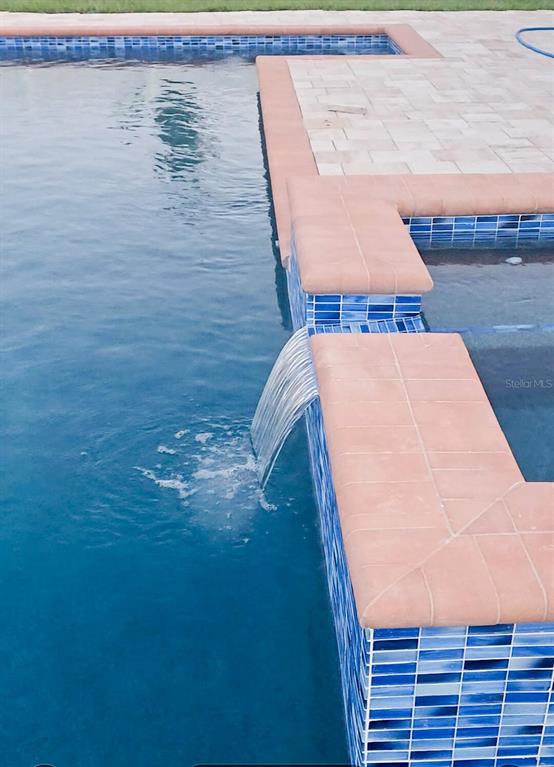 A spillover spa cascades water into a blue-tiled swimming pool with a stone paver deck — 1213 MICHELANGELO LANE, WINTER HAVEN, FL