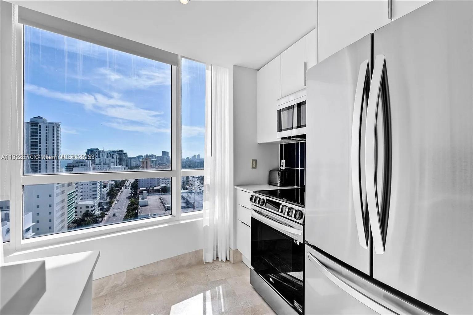 A modern kitchen features white cabinetry, stainless steel appliances, and a large window with city views — 4401 Collins Ave # 1604, Miami Beach FL 33140, MIAMI BEACH, FL