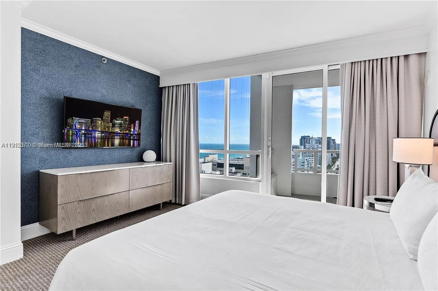 A bedroom features a blue textured accent wall, a television, and a balcony with ocean views — 4401 Collins Ave # 1604, Miami Beach FL 33140, MIAMI BEACH, FL