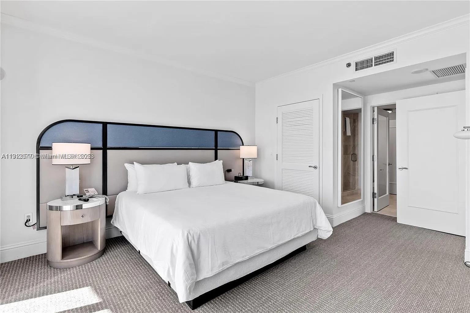 A bedroom features a king bed with a blue headboard, white bedding, and carpeted floors — 4401 Collins Ave # 1604, Miami Beach FL 33140, MIAMI BEACH, FL