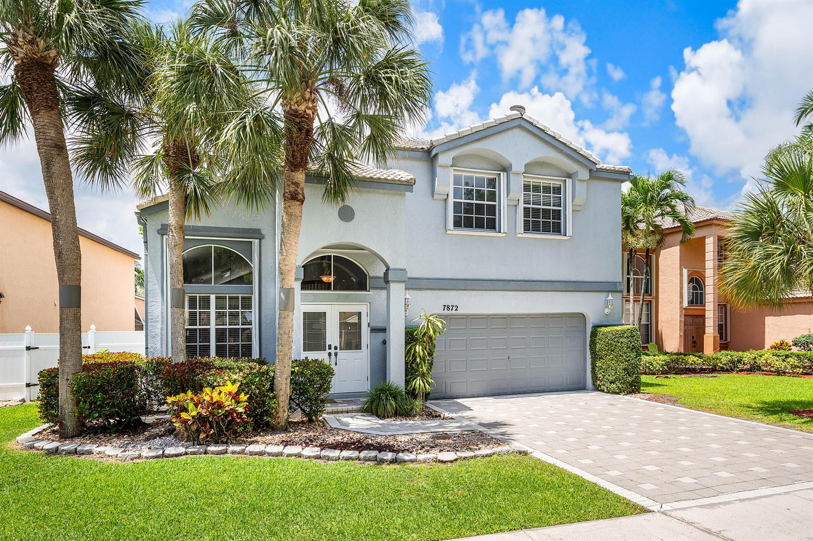 A two-story light blue house features a paved driveway, palm trees, and a two-car garage — 7872 Springvale Drive, Lake Worth FL 33467, LAKE WORTH, FL