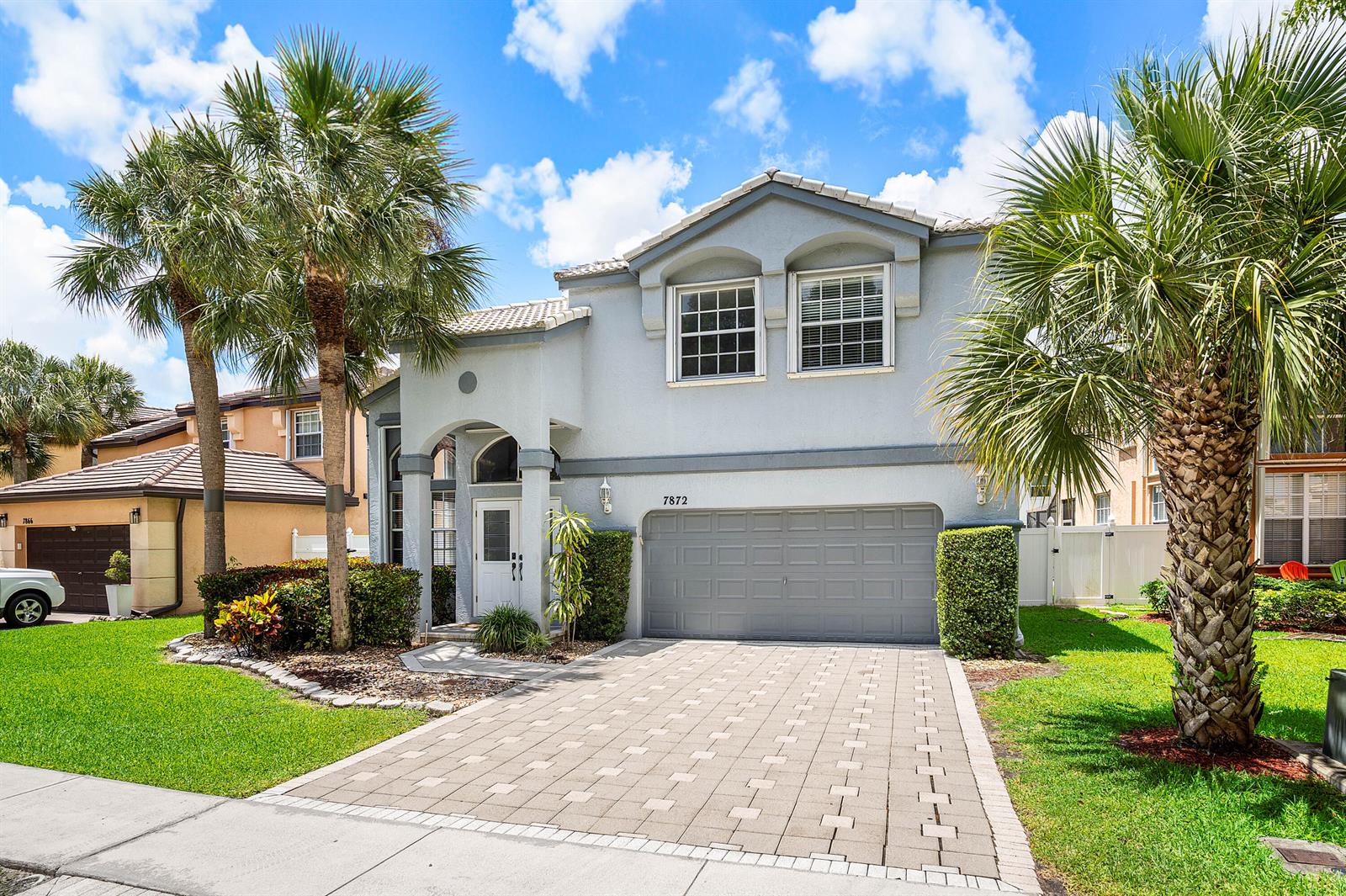 A two-story house with a gray stucco exterior, a paved driveway, and two palm trees — 7872 Springvale Drive, Lake Worth FL 33467, LAKE WORTH, FL