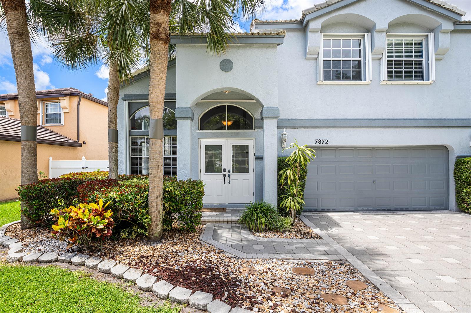 A two-story light blue house features a double front door, a garage, and palm trees — 7872 Springvale Drive, Lake Worth FL 33467, LAKE WORTH, FL