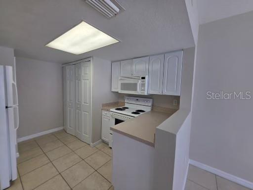 A kitchen features white cabinets, a white stove, a microwave, and light-colored tile flooring — 2419 FAN PALM DRIVE, DAVENPORT, FL