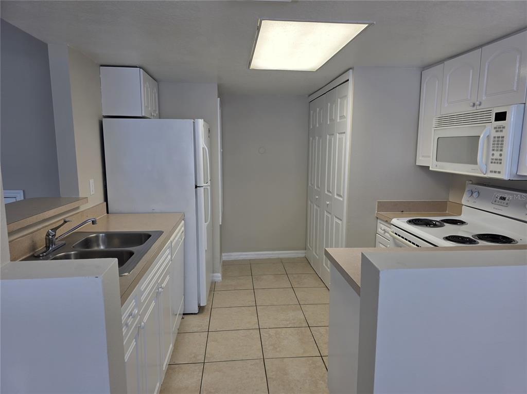 A kitchen features white cabinets, a white refrigerator, a double sink, and tiled flooring — 2419 FAN PALM DRIVE, DAVENPORT, FL