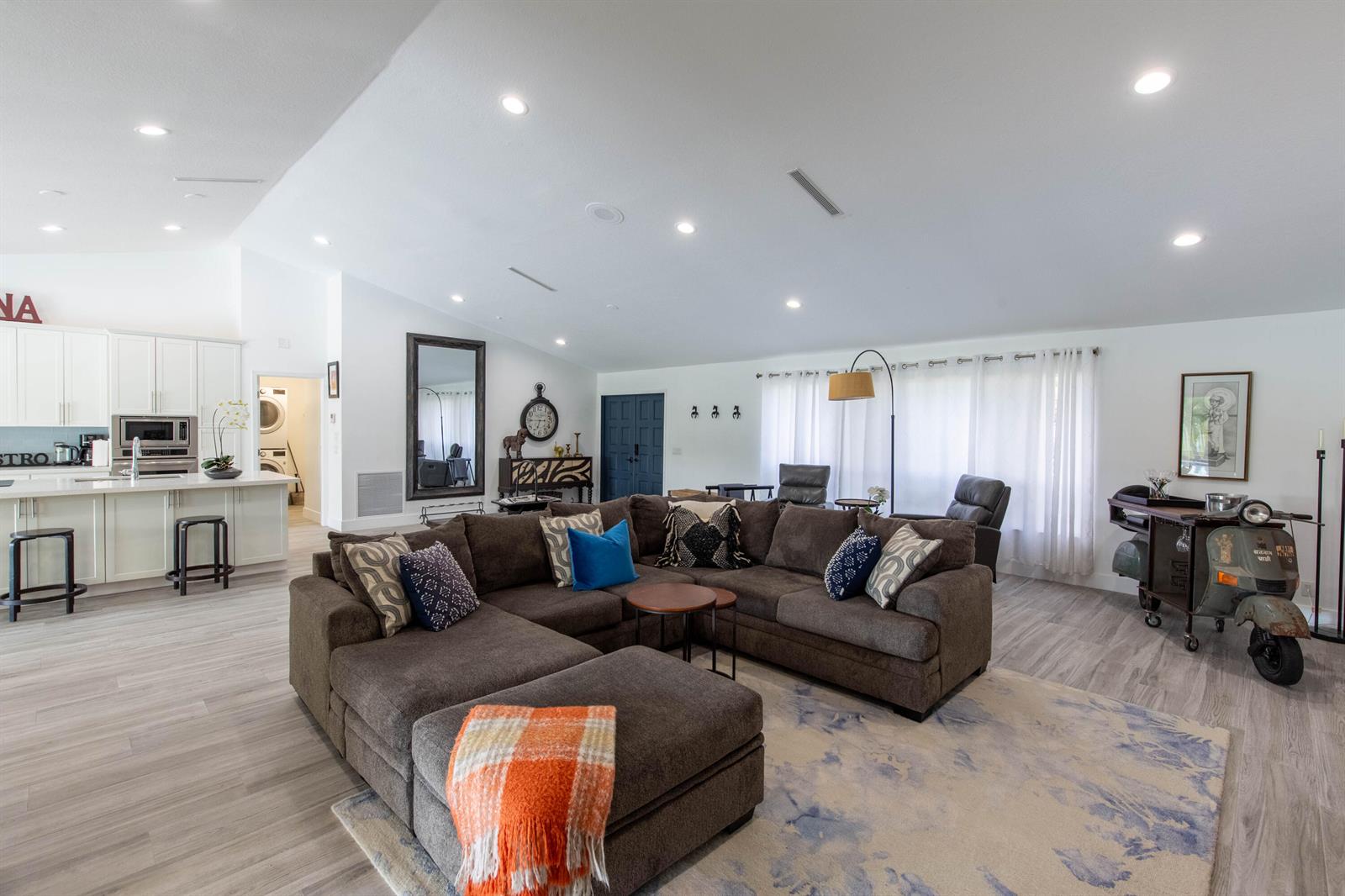 A large open-concept living room features a brown sectional sofa, kitchen island, and vintage scooter — 1327 Pine Valley Drive, Wellington FL 33414, WELLINGTON, FL