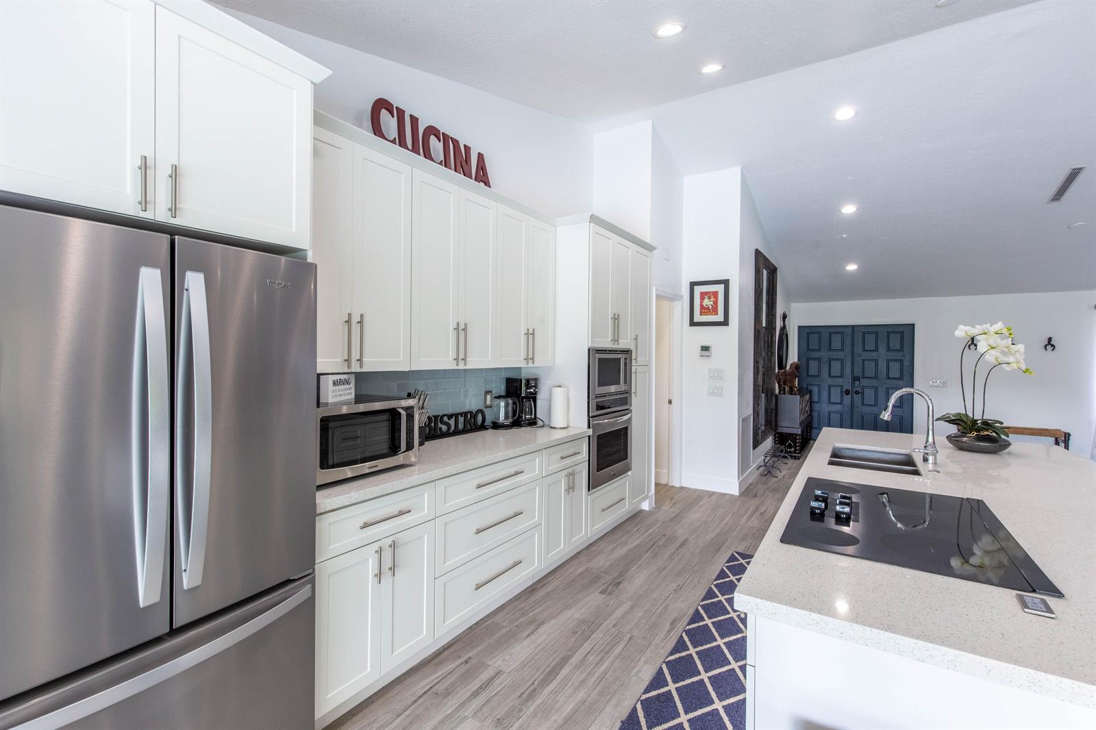 A modern kitchen features white cabinetry, stainless steel appliances, and a large central island — 1327 Pine Valley Drive, Wellington FL 33414, WELLINGTON, FL