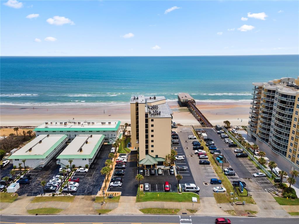An aerial view shows a beachside hotel, parking lots, and a pier extending into the ocean — 3647 S ATLANTIC AVENUE UNIT 6G, DAYTONA BEACH SHORES, FL