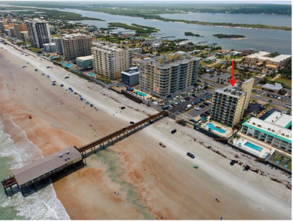An aerial view shows a beachfront condominium building next to a pier and the ocean — 3647 S ATLANTIC AVENUE UNIT 6G, DAYTONA BEACH SHORES, FL