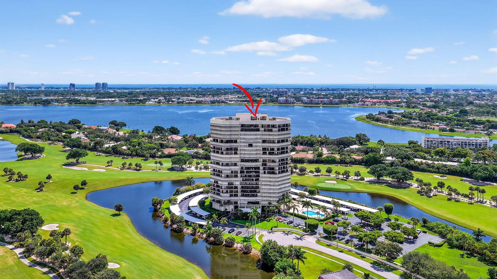 An aerial view of a high-rise residential building surrounded by a golf course and lake — 1900 Consulate Place # 1705, West Palm Beach FL 33401, WEST PALM BEACH, FL