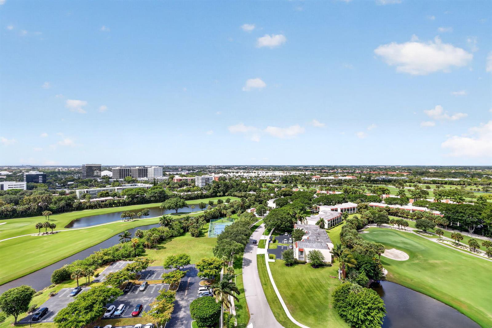 An aerial view shows a golf course, a parking lot, and residential buildings under a blue sky — 1900 Consulate Place # 1705, West Palm Beach FL 33401, WEST PALM BEACH, FL