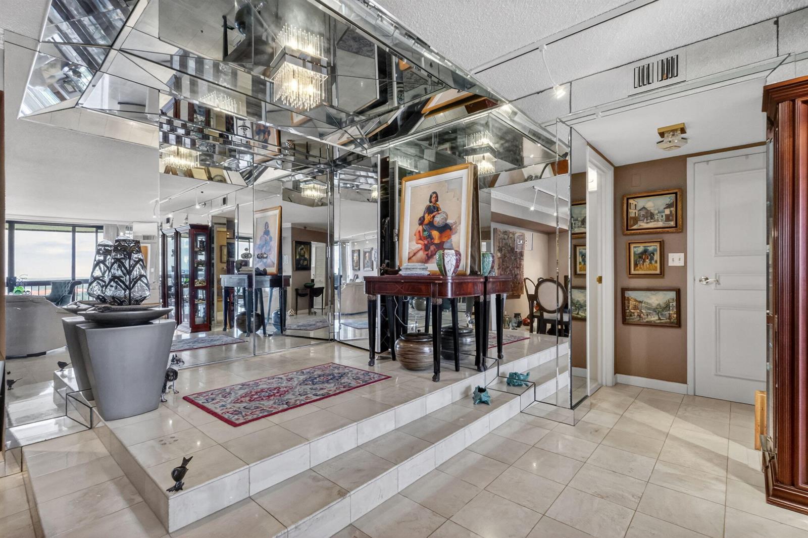 A foyer features a raised platform, mirrored walls, tile flooring, and a small area rug — 1900 Consulate Place # 1705, West Palm Beach FL 33401, WEST PALM BEACH, FL